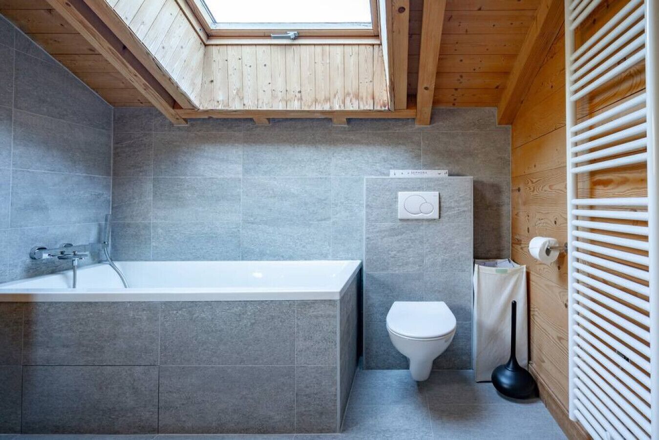 Une salle de bain moderne avec un puits de lumière, une baignoire, des toilettes et un radiateur.