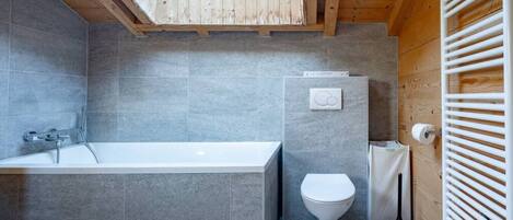 Une salle de bain moderne avec un puits de lumière, une baignoire, des toilettes et un radiateur.