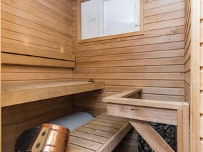 En sauna med trævægge, en bænk, et lille bord og et vindue med skodder.