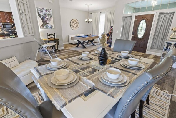 A dining area with a rectangular table set for four, surrounded by upholstered chairs with metallic studs. - The Black Porcupine | Private Pool | Pool Table & Arcade | Large Home | Child Friendly | Palm Coast (Palm Coast)