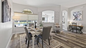 Comedor con una mesa lista para cuatro, un ventanal con persianas y vista al jardín.