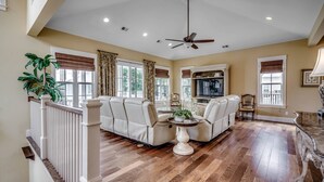 A spacious living room with a high ceiling, a ceiling fan, and a large window with curtains. - Stunning Home w Private Pool in North Beach Resort & Villas - Only 150 Yards to Pools/Beach! (North Myrtle Beach)