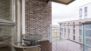 A balcony with a glass table and wicker chairs, a brick wall, and a view of other buildings.
