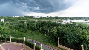 A view of a lush green landscape with a river, a bridge, and a building in the distance under a cloudy sky. - Urban Stay Service Apartment (Chengalpattu)