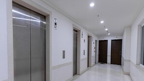 A clean, modern hallway with elevators and doors, featuring a tiled floor and white walls. - Urban Stay Service Apartment (Chengalpattu)