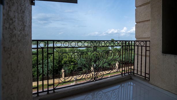 A balcony with a wrought iron railing, a view of greenery, and a clear sky. - Urban Stay Service Apartment (Chengalpattu)