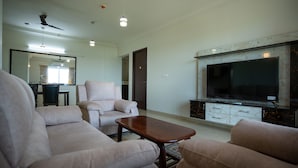A spacious living room with a large flat-screen TV, comfortable seating, and a ceiling fan. - Urban Stay Service Apartment (Chengalpattu)