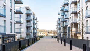 A modern residential building with balconies, a paved walkway, and a distant view of a mountain. - The Hunt Cherrywood (Laughanstown)