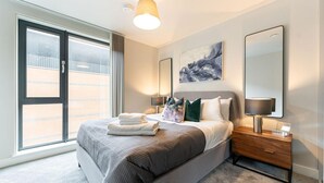 A modern bedroom with a large bed, bedside lamps, a painting, and a sliding glass door to the outside. - St Martin's Place - Birmingham City Centre (Birmingham)