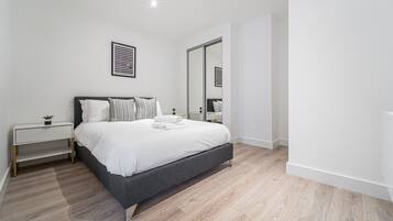 A modern bedroom with a bed, bedside tables, a mirror, and a small plant.