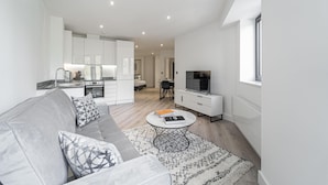 A modern living room with a grey sofa, a coffee table, and a TV on a white cabinet. - Sevenstays Residences Solihull - NEC / Airport (Solihull)