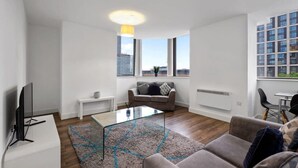 Uma sala de estar moderna com uma mesa de centro de vidro, um sofá, uma televisão e um espaço de jantar com mesa e cadeiras.