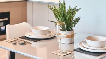 Cocina moderna con una mesa de comedor para dos personas, con cuencos blancos moteados, un vaso y un helecho en maceta.
