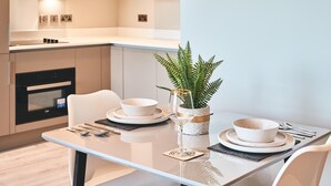 Une cuisine moderne avec des meubles blancs, un four encastré et un coin repas avec une table blanche mise pour deux personnes.