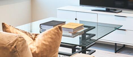 A modern living room with a sofa, a glass coffee table, a flat-screen TV, and a white cabinet.