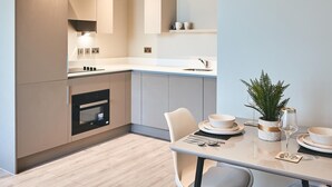 Une cuisine moderne dotée d’appareils électroménagers intégrés, un coin repas avec une table dressée pour deux personnes, et une petite plante en pot posée sur la table.