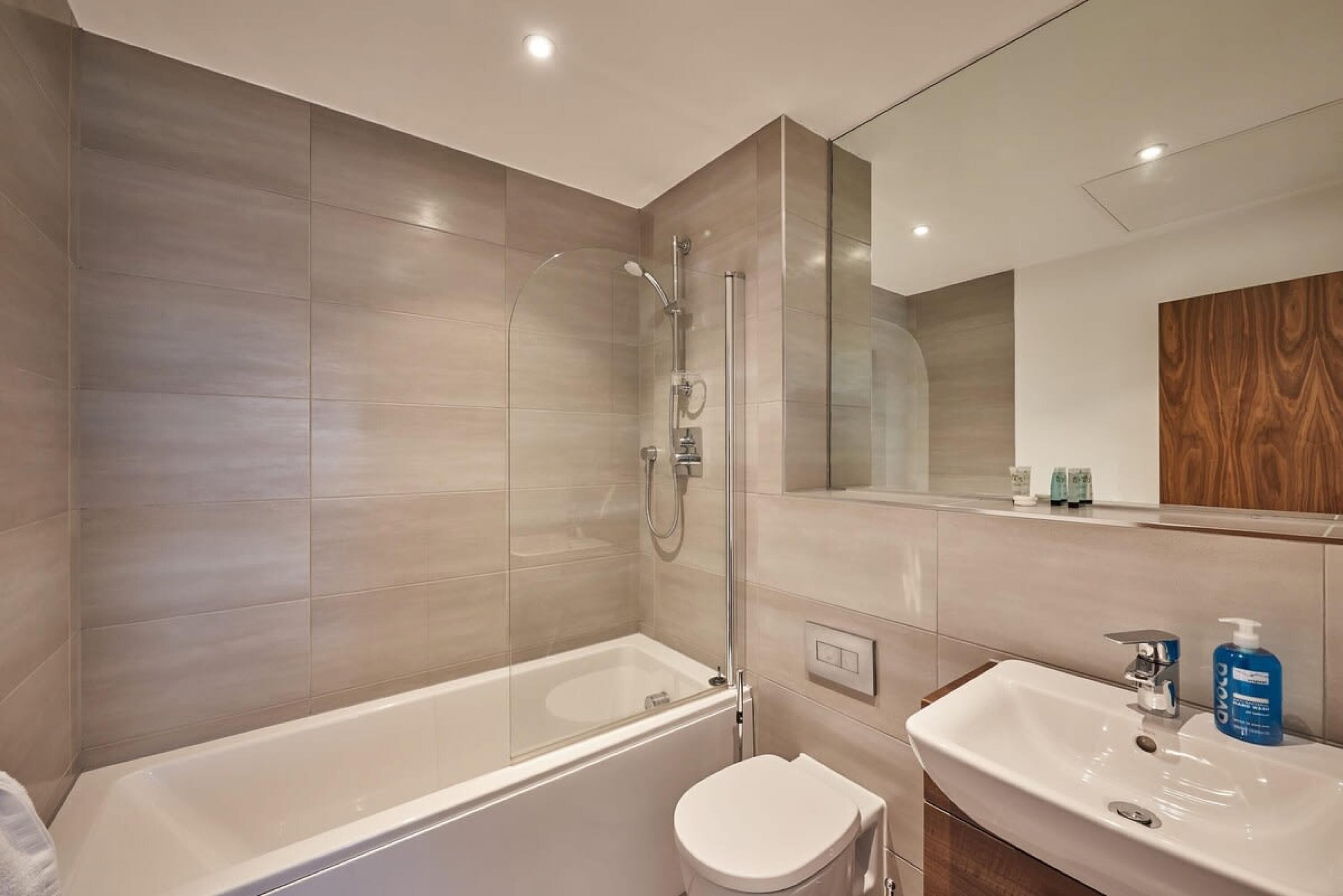 A modern bathroom with a glass-enclosed shower, a white bathtub, and a sink with a mirror above it.