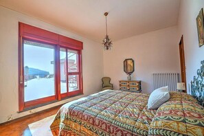 A bedroom with a large bed, a chandelier, a view through a sliding door, and a radiator.
