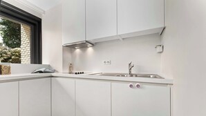 A modern kitchen with white cabinets, a stainless steel sink, and a window with a view of trees. - Sasea - ground floor apartment with garden (Nieuwpoort)