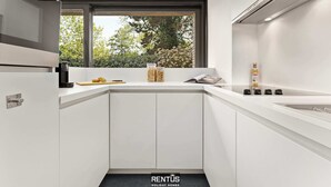 A modern kitchen with white cabinetry, a built-in stove, and a window overlooking greenery. - Sasea - ground floor apartment with garden (Nieuwpoort)