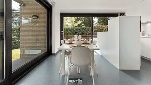 A modern kitchen with a dining area, large windows, and a view of greenery. - Sasea - ground floor apartment with garden (Nieuwpoort)