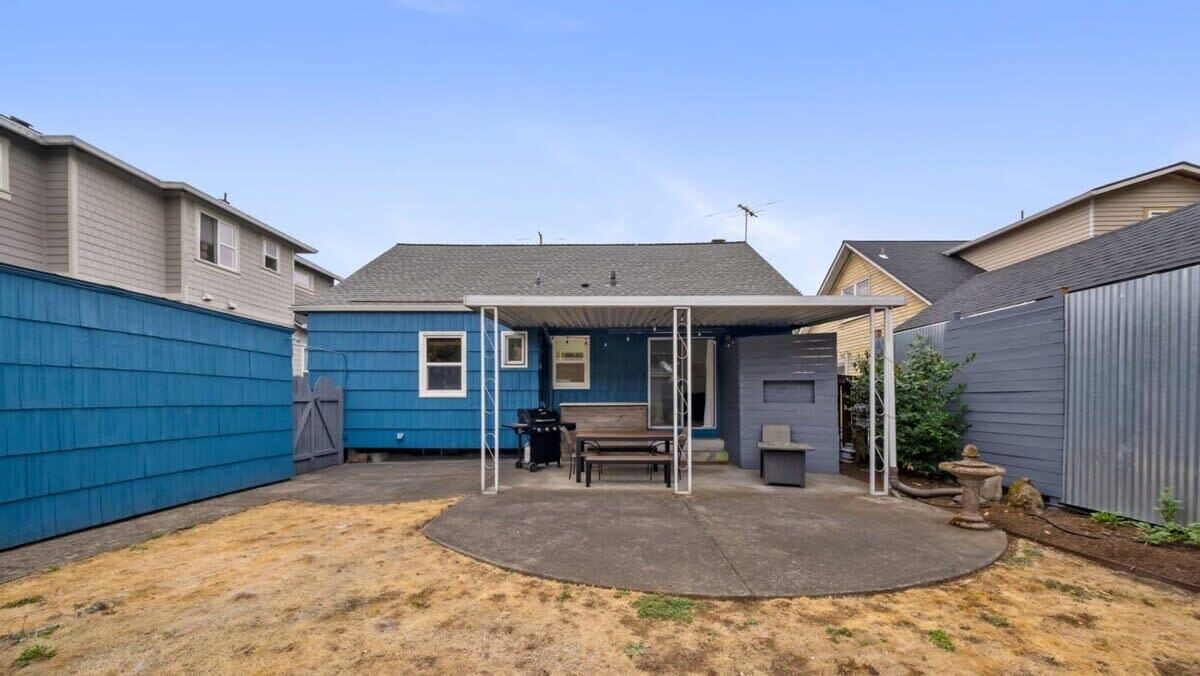 A backyard with a covered patio, a barbecue grill, and a wooden bench.