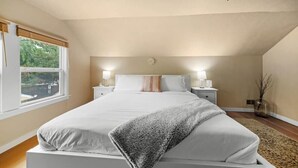 Un dormitorio con cama, mesitas de noche, un ventanal y vistas al verdor exterior.