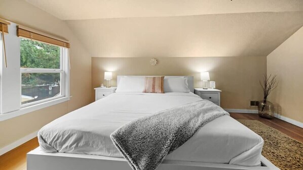 A bedroom with a bed, bedside tables, a window, and a view of greenery outside.