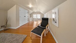 A spacious room with hardwood floors, a black chair, a small table, and a framed picture on the wall.