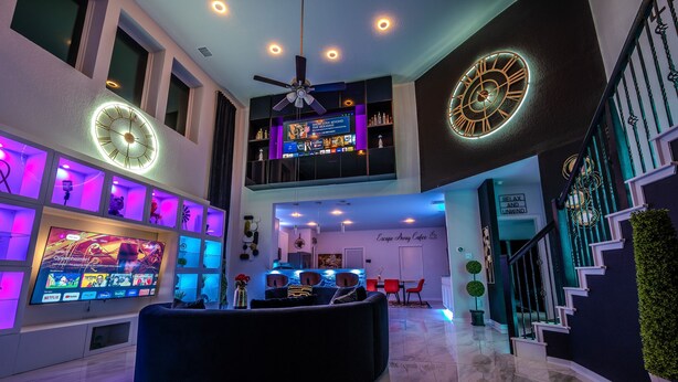 Amplia sala de estar con un mueble de entretenimiento grande, una zona de estar curvada y una escalera con un muro verde.