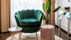 A room with a green armchair, a round table, and a small ottoman. There is a plant and a mirror on a console table. - Holt Old Town One Bedroom Apartments (Bucharest)