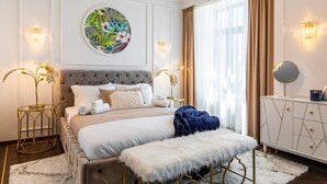 A bedroom with a tufted headboard, a round painting, two bedside tables with lamps, a dresser, and a large window with curtains. - Holt Old Town One Bedroom Apartments (Bucharest)