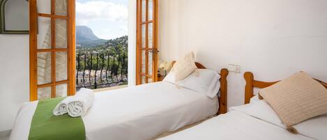 A hotel room with two beds, a balcony, and a mountain view.