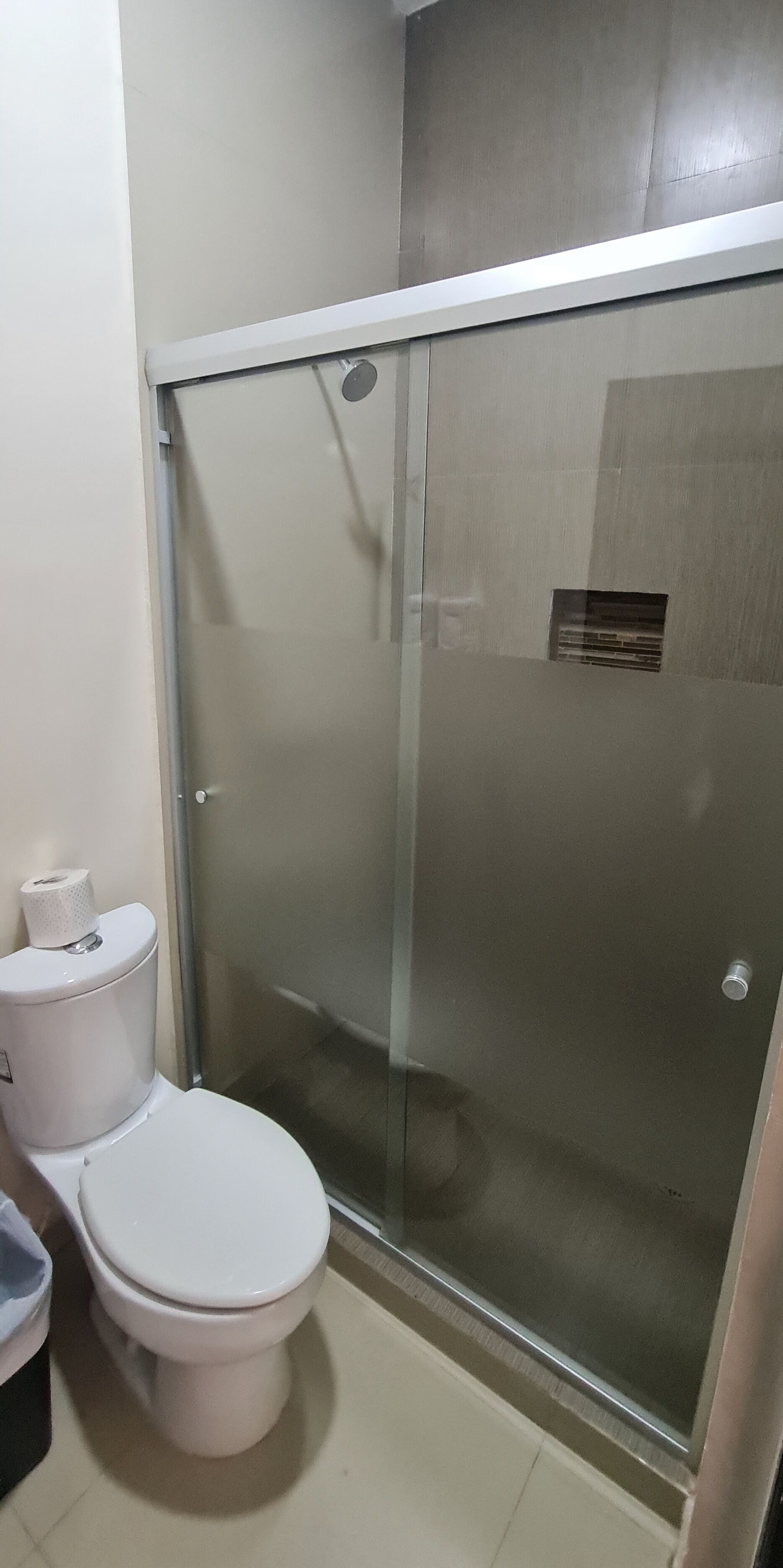 A bathroom with a toilet, a glass-enclosed shower, and a toilet paper roll.