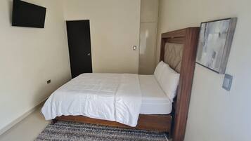 A bedroom with a bed, a door, a wall-mounted light, and a framed picture.