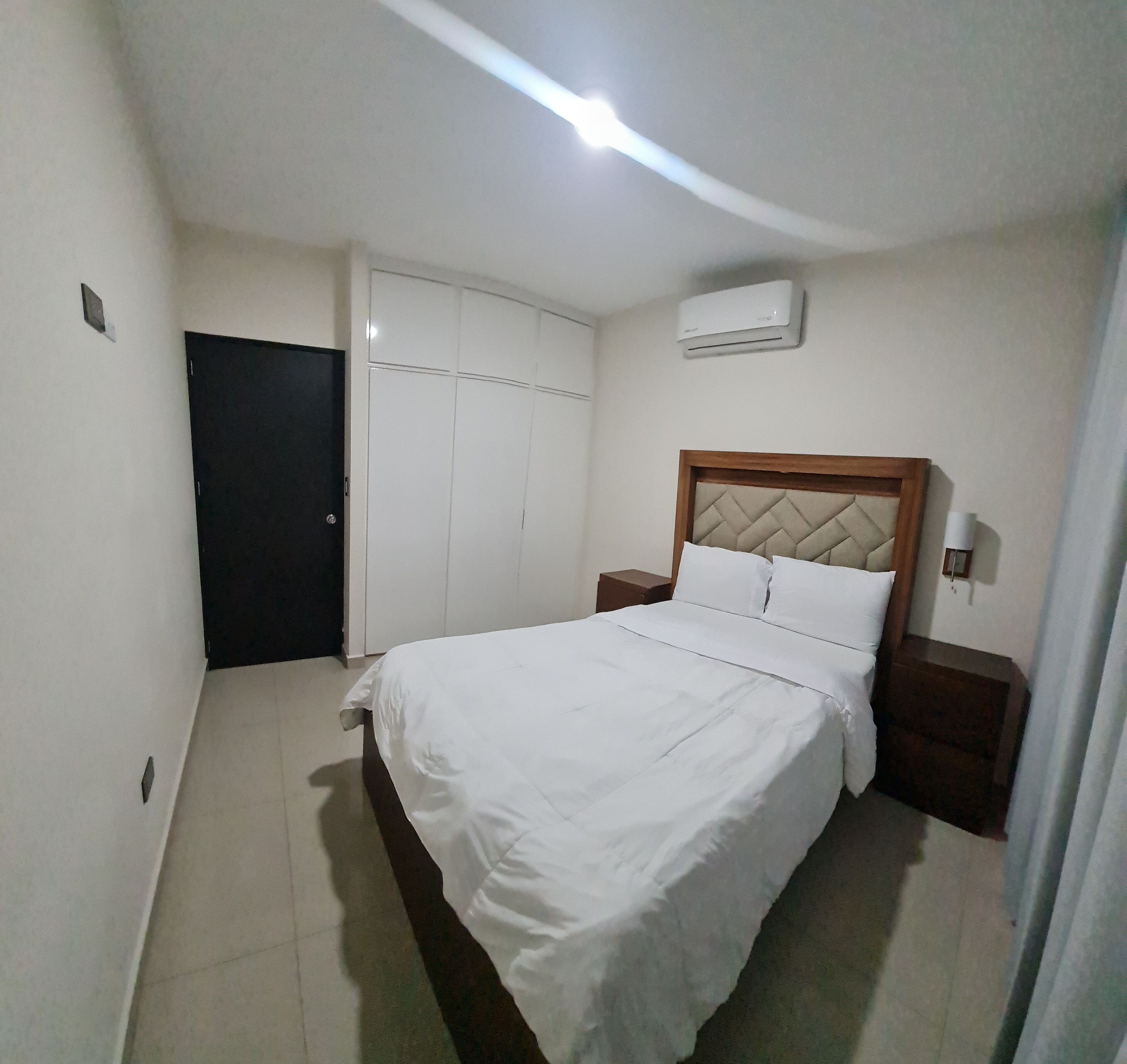 A bedroom with a bed, a wardrobe, a nightstand, and an air conditioning unit.