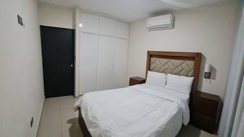 A bedroom with a bed, a wardrobe, a nightstand, and an air conditioning unit.