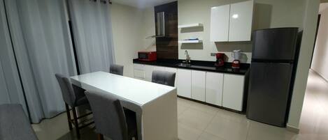 A compact kitchen with a white countertop, a black refrigerator, a microwave, and a coffee maker.