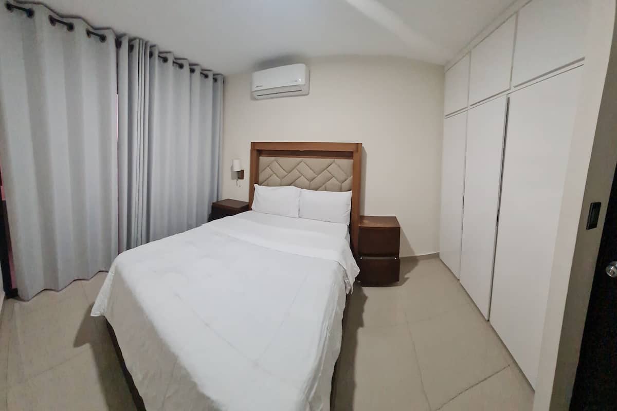 A hotel room with a bed, nightstands, an air conditioner, and a wardrobe.