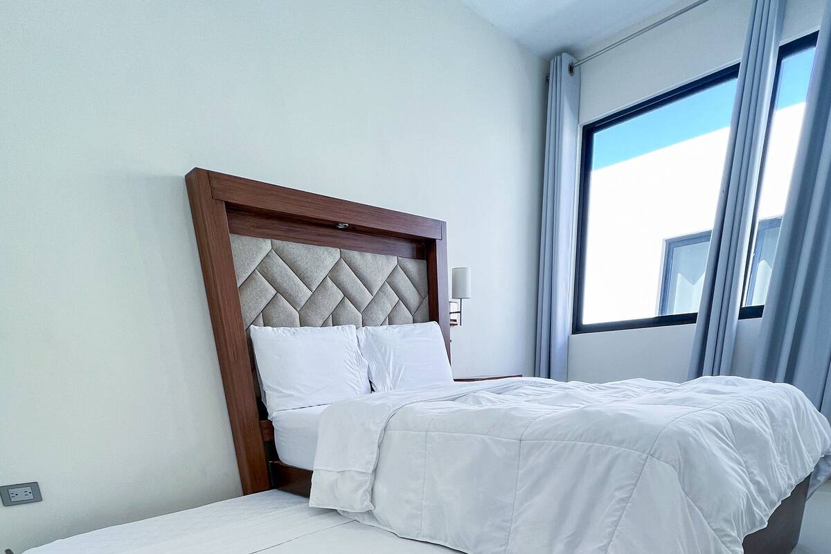 A modern hotel room with a large bed, a wooden headboard, and a large window with curtains.