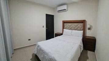 A bedroom with a bed, a nightstand, a wall-mounted air conditioner, and a door.