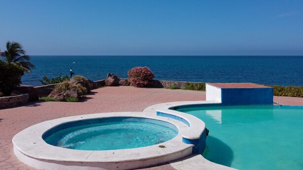 Ein Pool mit geschwungener Form, umgeben von einem Steinpfad und Blick auf den Ozean.