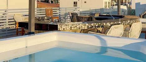 Una piscina en la azotea con sillas de descanso y vistas a edificios y una montaña.