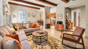 A spacious living room with a sofa set, a coffee table, and a chair. There is a kitchen in the background with wooden cabinets and a dining area. - Desert Daydream A | 1BR Legacy Villa (La Quinta)