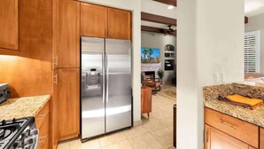 A modern kitchen with wooden cabinets, a stainless steel refrigerator, a gas stove, and a granite countertop. - Desert Daydream A | 1BR Legacy Villa (La Quinta)