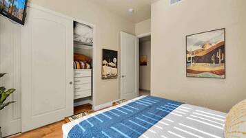 A bedroom with a bed, a wardrobe, a painting, and a television on the wall.