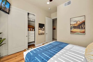 A bedroom with a bed, a wardrobe, a painting, and a television on the wall.