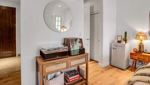 Une pièce comprenant une console en bois sur laquelle sont posés des disques et des livres, un miroir rond accroché au mur et une petite armoire avec une lampe.