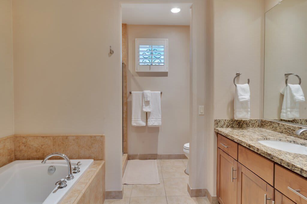 A bathroom with a bathtub, a sink, and a window with blinds.