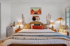A neatly arranged bedroom with a large bed, a headboard with decorative elements, two bedside lamps, and a wall-mounted painting.